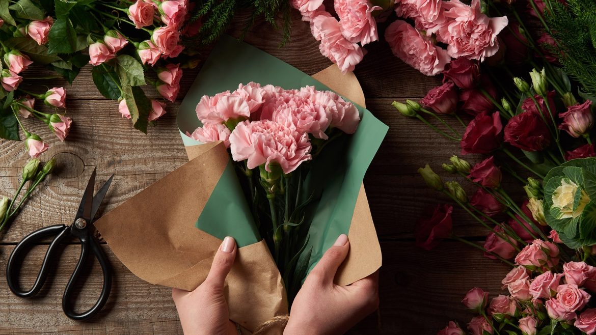 Hands arranging pink flowers on a rustic table, flowers theme