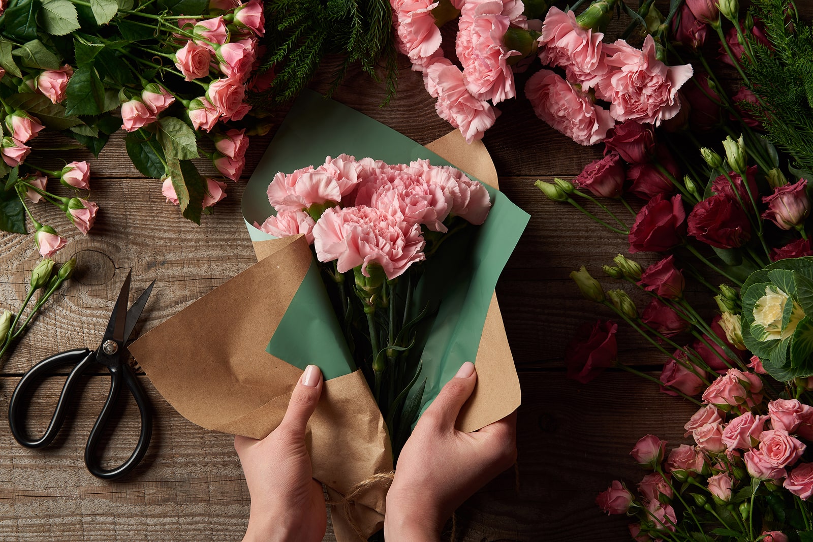 Hands arranging pink flowers on a rustic table, flowers theme