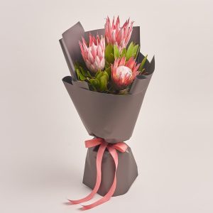 Elegant bouquet of pink protea flowers wrapped in gray paper